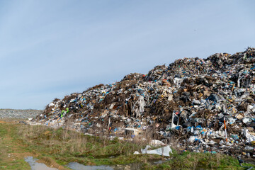 Landfill Overflowing with Trash and Debris Under Blue Sky, Illustrating Environmental Pollution and...