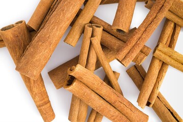 Close-up of dried cinnamon bark fragments on white, capturing their natural curves and rugged surfaces.