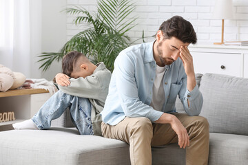 Thoughtful young father and his sad little son sitting on sofa after squabbling at home