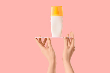 Woman holding bottle of sunscreen cream with surfboard on pink background
