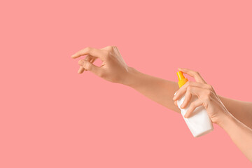 Woman applying sunscreen cream on her hand against pink background