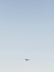 Obraz premium An aircraft flying in a clear blue sky. The aircraft is seen as a silhouette against the bright backdrop. Minimalist composition with a focus on aviation and flight.