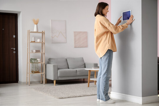 Young happy woman using smart home security system control panel on wall in room - Powered by Adobe
