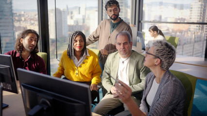 Diverse professional team analyzing complex business data while collaborating near computer, city skyline visible through expansive office window during strategic meeting