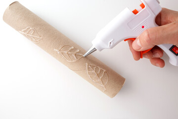 Hand using hot glue gun to create leaf pattern on cardboard tube. close-up shot. DIY crafting and...