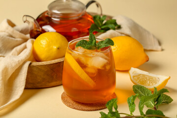 Teapot and glass of lemon ice tea with mint on beige background, closeup