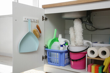 Baskets and bucket with different cleaning supplies and paper towels under sink in kitchen