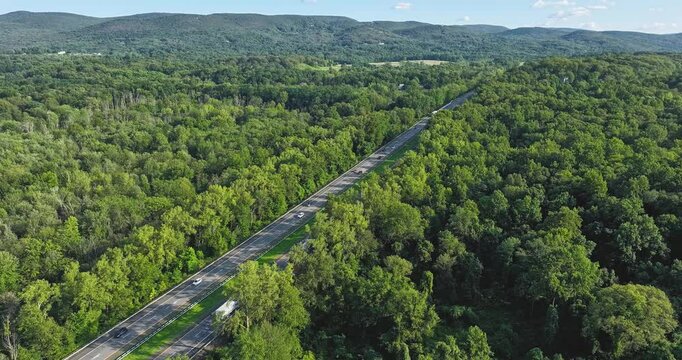 Daytime aerial hyperlapse video over a stretch of interstate, highway, through a green vegetative area. 