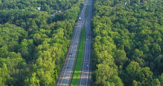Daytime aerial hyperlapse video over a stretch of interstate, highway, through a green vegetative area. 
