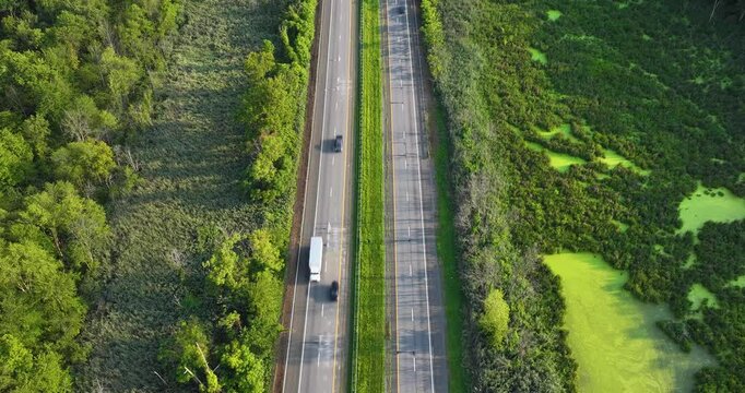 Daytime aerial hyperlapse video over a stretch of interstate, highway, through a green vegetative area. 