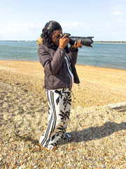 Calshot Hampshire England UK. 27.04.2025. African woman using an DSLR digital camera while on a visit to Calshot beach in Hampshire UK
