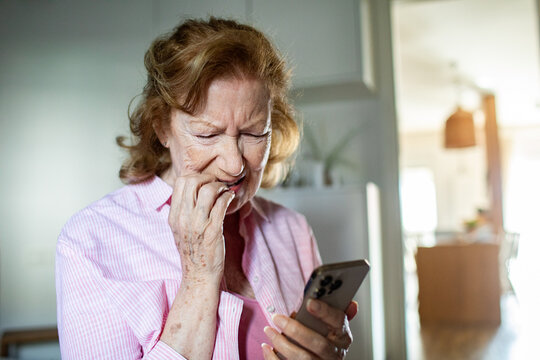 Worried senior woman reading stressful news on smartphone at home