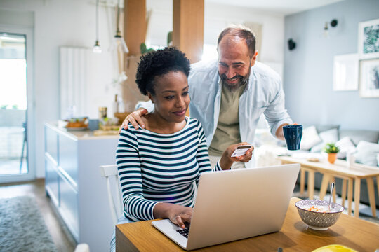 Happy couple shopping online with credit card at breakfast table