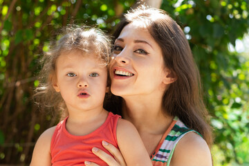 Beautiful happy smiling mother hugging with love her cute daughter on nature green trees sunny summer background. Happy family. Closeup natural real emotion portrait 