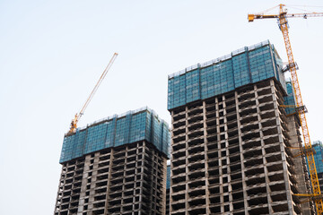 Tall unfinished skyscrapers with cranes during high-rise construction phase