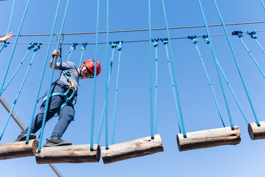 Child boy in Protective Gear Navigating a High Ropes Course in adventure park Against Blue Sky
