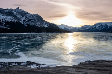Frozen Abraham Lake reflects sunset over snow-capped mountains in winter landscape