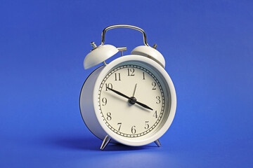 One white alarm clock on blue background