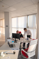 Caucasian man standing at colleague's desk discussing work. 