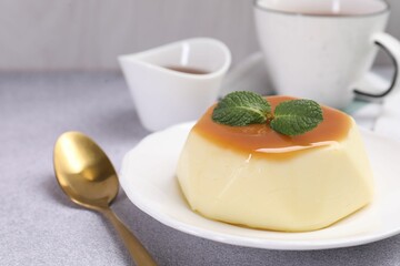 Delicious pudding with caramel sauce and mint served on light table, closeup