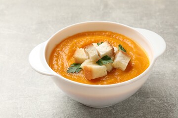 Tasty pumpkin cream soup with croutons and parsley in bowl on grey textured table, closeup