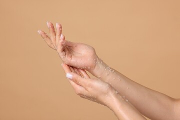 Woman applying body scrub onto her hands on beige background, closeup