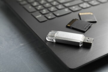 Usb flash drive, SD memory cards and laptop on grey textured table, closeup