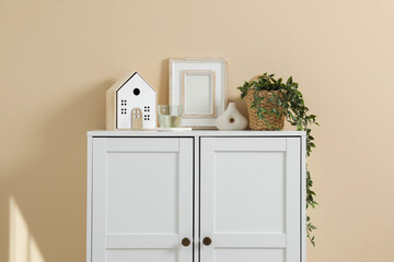 Dresser with stylish decor and houseplant near beige wall indoors