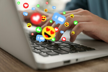 Woman using laptop at table, closeup. Social media notifications (likes, messages and emojis)...