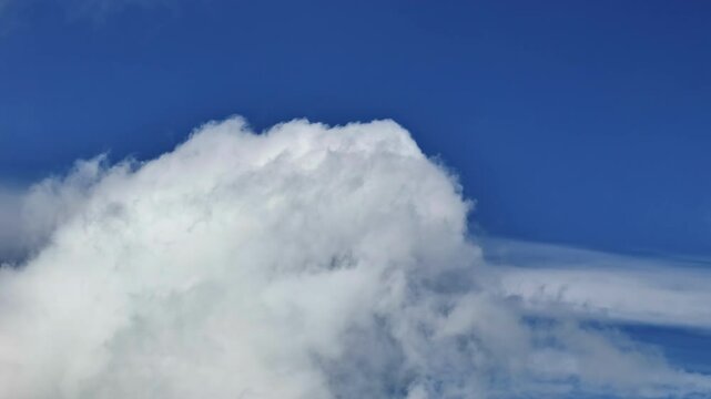 Large cumulus cloud rises against a deep blue sky with layers of soft white vapor drifting