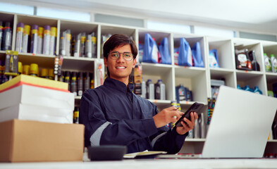 Mechanic managing inventory using mobile device and laptop in auto shop