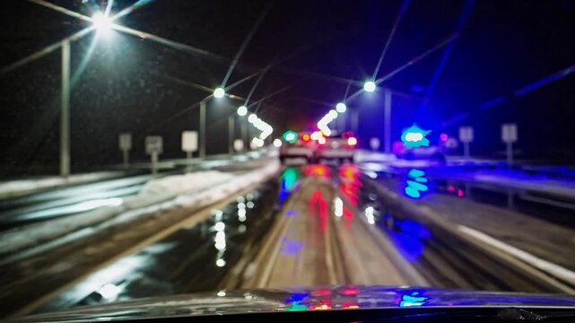 Driver&rsquo;s night view approaching police checkpoint in snowy road, blurred flashing blue and red lights symbolizing safe driving.

