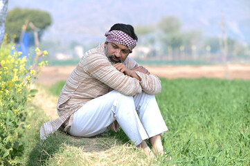 Indian sad and discouraged farmer man sitting in crop farmland and lost deeply his agriculture...