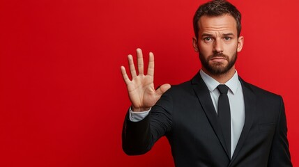 Businessman in black suit gestures with hand against red backdrop.