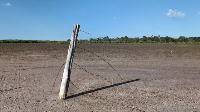 Wooden fence post with broken rusty wires in a mudflat dirt field