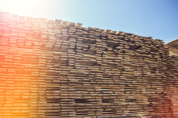 A large stack of lumber boards is neatly stacked at a lumber yard. The boards are arranged in a uniform pattern, with the grain running vertically.