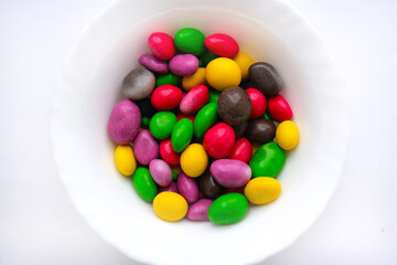 Glazed peanuts of different colors on a plate, white background. Multicolored peanuts. close-up. Snack colored kernel, hazelnut, nut.