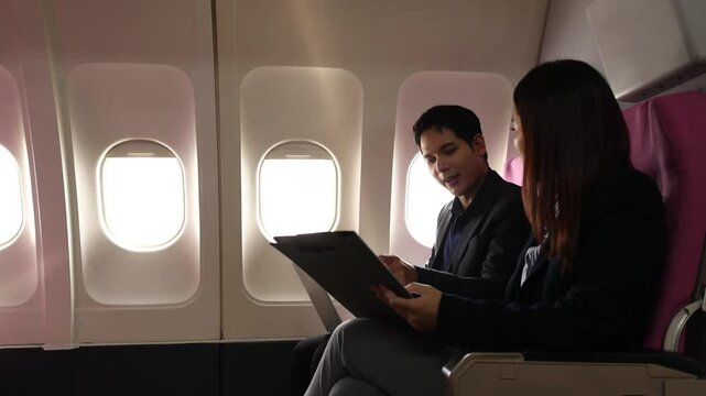 businessman and his secretary discuss sales paper while traveling by plane to sign a contract with another company, during the business trop of the two businessmen they double-checked to be sure