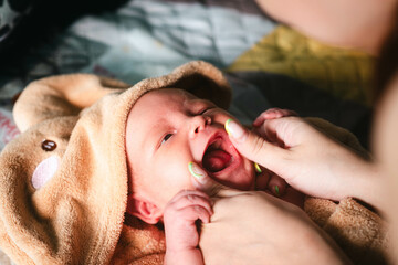 Newborn lying in towel after bathing. Anonymous mom playing with infant.
