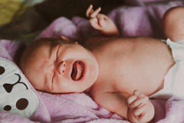 Newborn screaming, lying on towel after bathing. Portrait of crying infant, showing discontent.