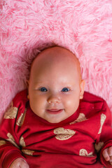 Portrait of a newborn girl in a red hoodie on a pink background