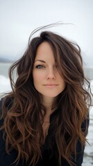 Naklejka premium A woman with long, wavy brown hair partially covering her face, looks directly at the camera outdoors