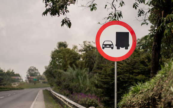 Se&ntilde;al de tr&aacute;nsito de prohibido adelantar en carretera rural, rodeada de vegetaci&oacute;n, con cielo nublado y perspectiva de v&iacute;a libre en segundo plano