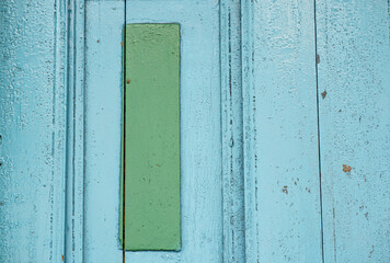 Primer plano de una puerta de madera pintada de azul con un rectángulo verde al centro, texturas desgastadas y estilo vintage.