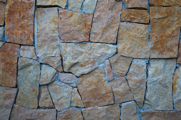 A wall made of uneven stones in sandy shades with blue seams creates a natural texture....