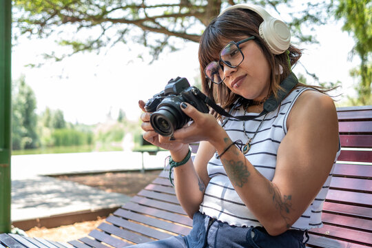 Photographer reviewing digital images on camera, wearing headphones, seated on urban park bench - Powered by Adobe