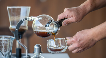 A person is pouring coffee into a cup from a glass container