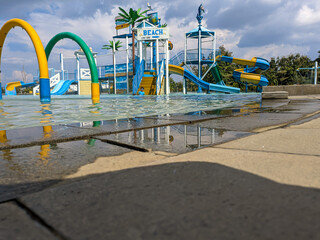 Fototapeta premium Outdoor recreation focused on the poolside with a blurred background of rides at a crowded water park with clear pool water. Summer time, waterboom.