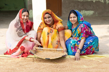 Indian rural women using a winnowing basket strainer to clean the wheat grain. Indian rural women...