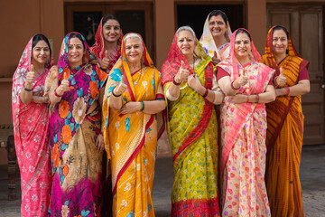 Women Empowerment in India. 
A group of Indian rural women showing thumbs up in colorful traditional dresses posing in front of the camera at village. Unity of Rural women in India.